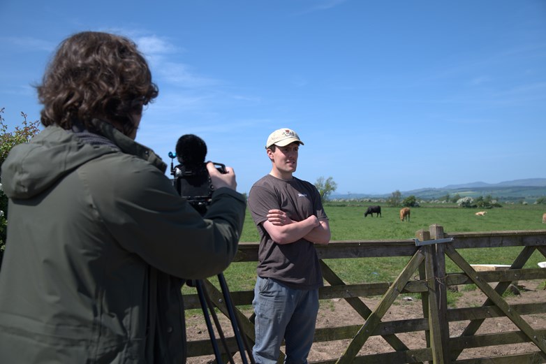 Man on a farm being filmed for a video.