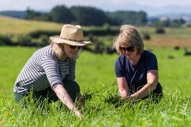 2 women squatting in a paddock, analysing the grass.